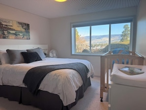 Une chambre avec un lit, une fenêtre donnant sur l’extérieur, un ventilateur et une petite table avec un livre.