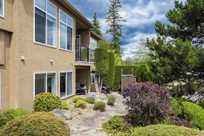A two-story building with a stone pathway, a balcony, and various shrubs.