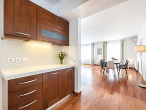 A modern kitchen with wooden cabinets, a white countertop, and a dining area with a table and chairs.