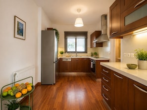 A modern kitchen with wooden cabinets, a stainless steel refrigerator, and a window providing natural light. - Adelos III Bloom Villa – 5BR 360m² - Sauna - Rooftop (Elliniko)