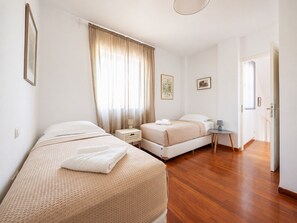 A hotel room with two beds, a bedside table, a chair, and a door leading to another room. - Adelos III Bloom Villa – 5BR 360m² - Sauna - Rooftop (Elliniko)