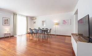 A modern living room with a dining area, wooden flooring, a flat-screen TV, and artwork on the walls. - Adelos III Bloom Villa – 5BR 360m² - Sauna - Rooftop (Elliniko)