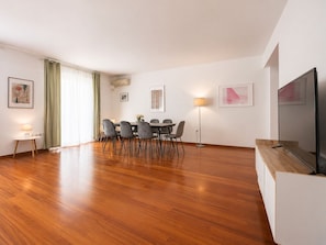 A modern living room with a dining area, wooden flooring, a flat-screen TV, and artwork on the walls. - Adelos III Bloom Villa – 5BR 360m² - Sauna - Rooftop (Elliniko)
