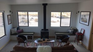 A cozy living room with a fireplace, large windows, a sofa, and a coffee table. - Huge Views in North Joshua Tree w/ Outdoor Bathtub & Shower (Joshua Tree)