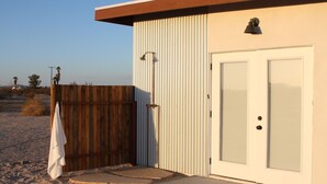 A building with a corrugated metal exterior, a wooden door, and a small porch area with a towel hanging on the door. - Huge Views in North Joshua Tree w/ Outdoor Bathtub & Shower (Joshua Tree)