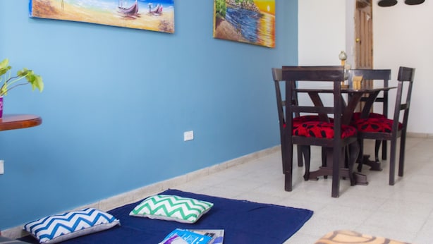 Un comedor con pared azul, dos cuadros, una mesa con sillas y una alfombra azul.