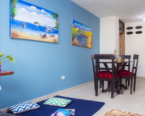 Ein Essbereich mit blauer Wand, zwei Gemälden, einem Tisch mit Stühlen und einem blauen Teppich.