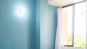 Un dormitorio con cama, mesita de noche, ventana con cortina y lámpara de pared.