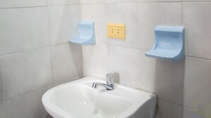 Un baño con un lavamanos blanco, un espejo redondo y dos dispensadores de jabón azules en la pared.