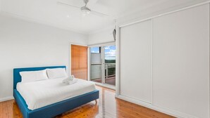 Une chambre à coucher avec un lit, un ventilateur de plafond et une porte-fenêtre coulissante donnant sur un balcon.