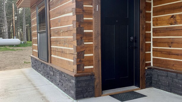 A log cabin with a black door and windows, a concrete driveway, and a stone foundation. - {Big Timbers} Lodging next to North Entrance of Itasca State Park (Shevlin)