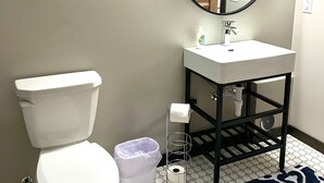 A bathroom with a toilet, sink, mirror, and a trash bin. - {Big Timbers} Lodging next to North Entrance of Itasca State Park (Shevlin)