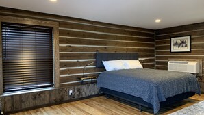 A bedroom with a wooden wall panel design, a bed with a grey bedspread, a bedside table, a lamp, and a framed picture on the wall. - {Big Timbers} Lodging next to North Entrance of Itasca State Park (Shevlin)