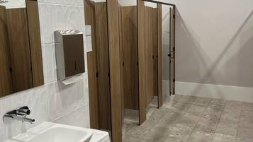 Un baño moderno con lavamanos blanco, espejo y separadores de madera para mayor privacidad.
