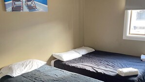 Two single beds with dark bedding and white pillows, a window with blinds, and a painting of a beach scene on the wall. - Australian Hotel Young (Young)