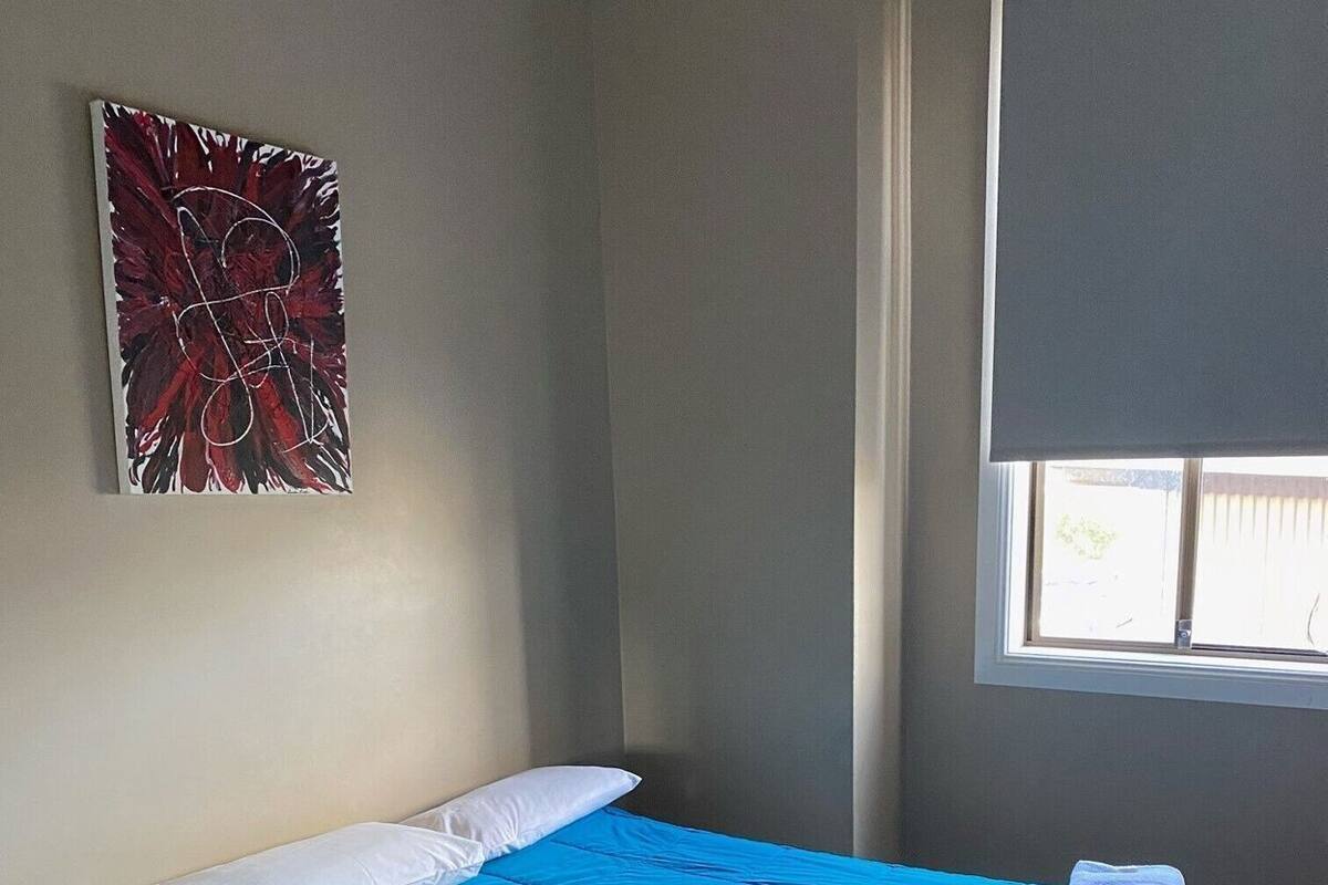 A single bed with a blue bedspread, white pillows, and a folded towel on the side.