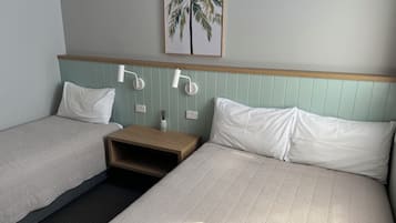 Habitación de hotel con dos camas, una mesita de noche, una lámpara de pared y un cuadro con una palmera.