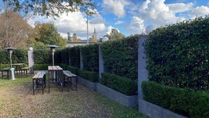 An outdoor patio area with tables and chairs, surrounded by neatly trimmed hedges and a stone wall. - Australian Hotel Young (Young)