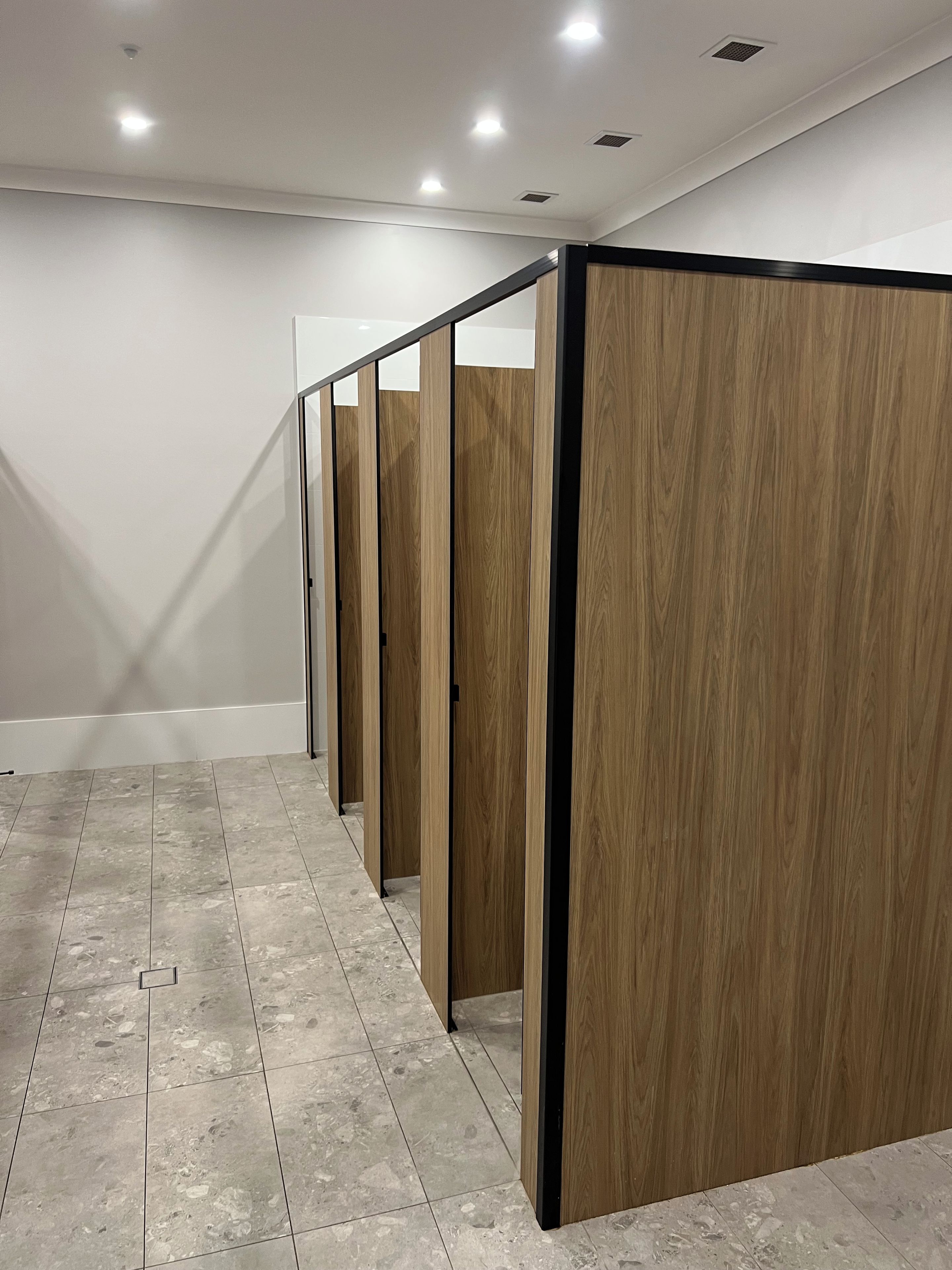 A row of wooden partitioned rooms with a tiled floor and recessed ceiling lighting.
