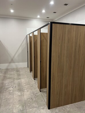 A row of wooden partitioned rooms with a tiled floor and recessed ceiling lighting.