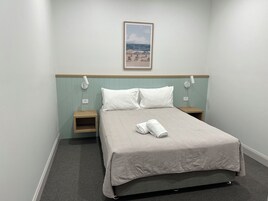 Habitación de hotel con cama, dos mesitas de noche, lámpara de pared, enchufe y un cuadro con una playa.