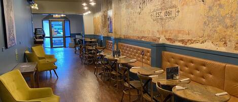 Interior de un restaurante con mesas de madera y sillas amarillas, una pared con la señalización 'Shamrock Inn' y vista de la calle.