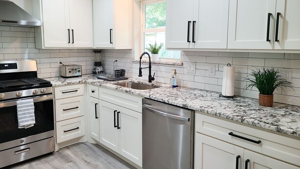 A modern kitchen with white cabinets, stainless steel appliances, a granite countertop, and a window providing natural light. - Stylish design,king bed, fast WiFi. Safe, tranquil, minutes from central Dallas. (Dallas)