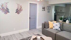 A living room with a gray sofa, decorative wall art, a ceiling fan, and a door leading to a kitchen. - Stylish design,king bed, fast WiFi. Safe, tranquil, minutes from central Dallas. (Dallas)
