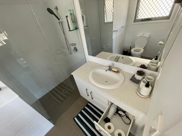 Un baño moderno con cabina de ducha de vidrio, lavabo blanco con espejo y retrete.