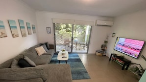 A living room with a grey sofa, a coffee table, a TV, and a sliding glass door leading to an outdoor area.