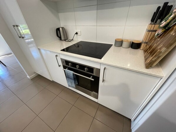 A modern kitchen with white cabinetry, a black stovetop, and a built-in oven. There are wooden utensils and a kettle on the countertop.