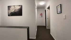 A hallway with a framed picture on the left, a framed notice on the right, and a door at the end.