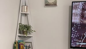 A living room with a white bookshelf, a television, a woven basket, and a potted plant.