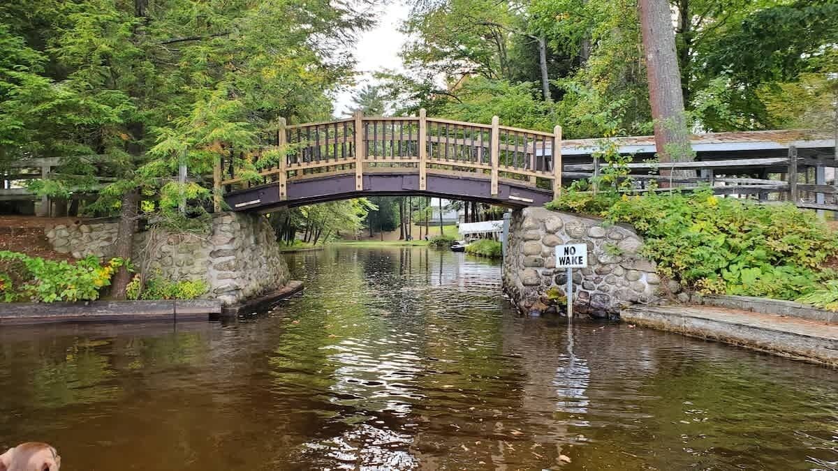 Un pont en bois enjambant une étendue d’eau paisible, entouré d’une végétation luxuriante et de murs de pierre.