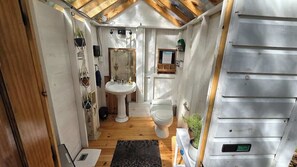 Un baño pequeño con suelo de madera, un lavamanos blanco, un inodoro y una ventana.