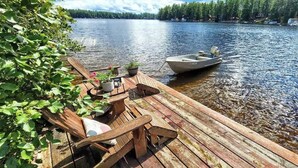 Une jetée en bois, avec des chaises et un petit bateau, d’où l’on peut admirer un lac paisible bordé d’arbres.