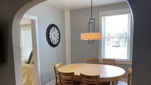 A dining area with a round table and chairs, a wall clock, and a window with blinds. - Downtown Lakeside in Muskegon-by local businesses,10 min to beach, Htub seasonal (Muskegon)