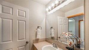 Une salle de bain avec un lavabo blanc, un miroir avec éclairage intégré et une orchidée en pot.