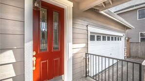Une porte de garage d’habitation, une porte rouge avec un panneau en verre, et un petit espace de porche doté d’une rambarde en métal.