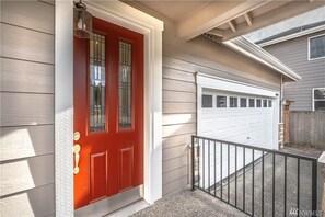 Stylish home with a prominent red door, flanked by a small porch and garage.