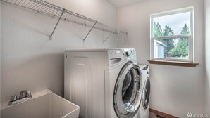 Une buanderie équipée d’un lave-linge et d’un sèche-linge à chargement frontal, d’une petite fenêtre et d’une étagère en métal au-dessus du lave-linge.