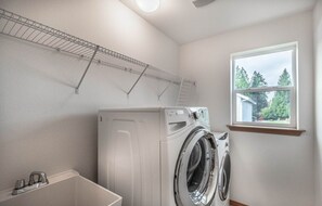 Une buanderie équipée d’un lave-linge et d’un sèche-linge à chargement frontal, d’une petite fenêtre et d’une étagère en métal au-dessus du lave-linge.