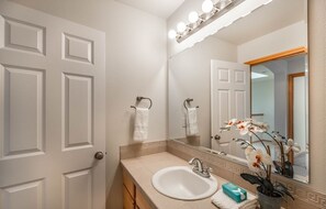 Une salle de bain avec un lavabo blanc, un miroir avec éclairage intégré et une orchidée en pot.