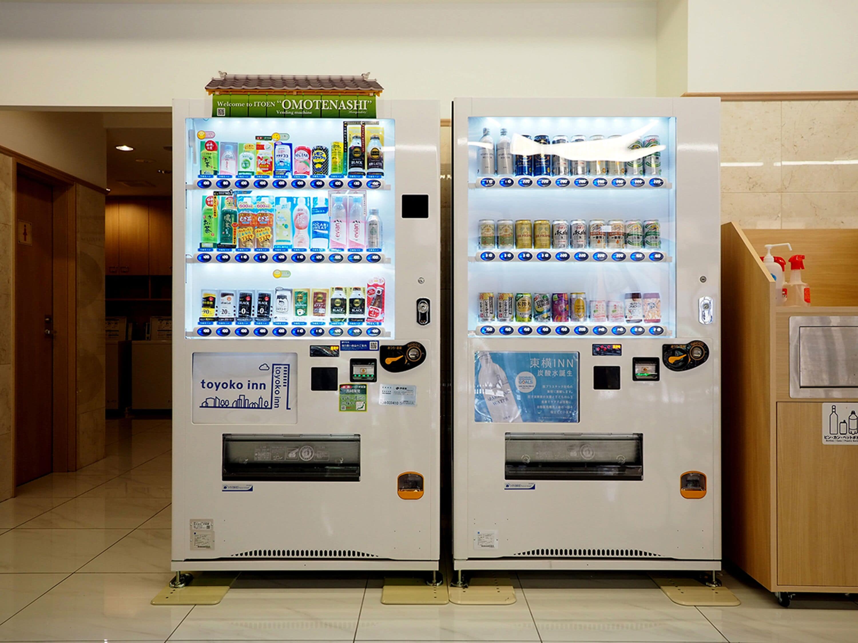Two vending machines in a hallway with a wooden cabinet and a tiled floor.