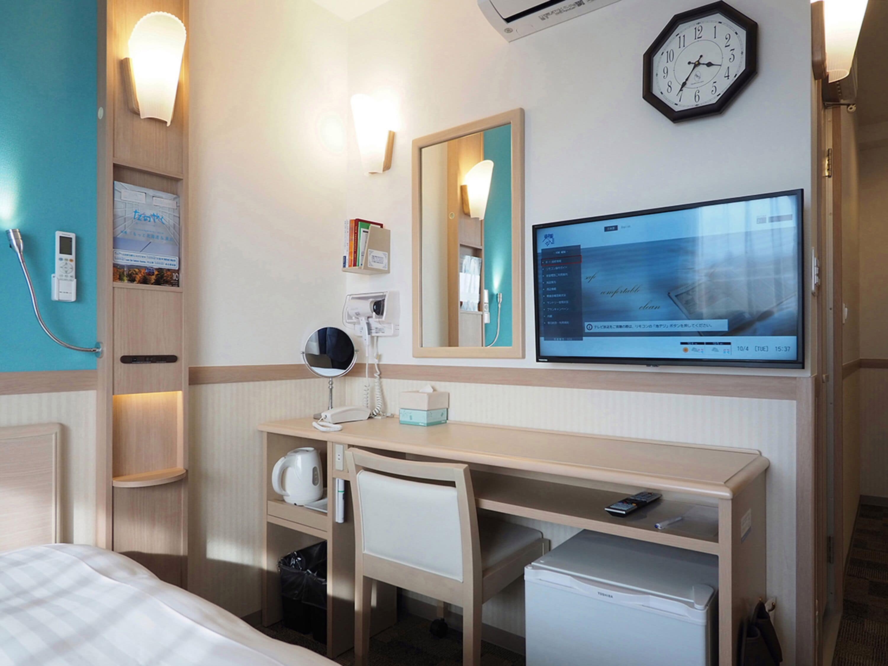 A hotel room with a bed, desk, chair, and a television displaying a menu.