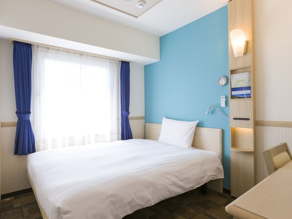 A hotel room with a large bed, a desk, a chair, a nightstand, a wall clock, and a wall-mounted lamp.