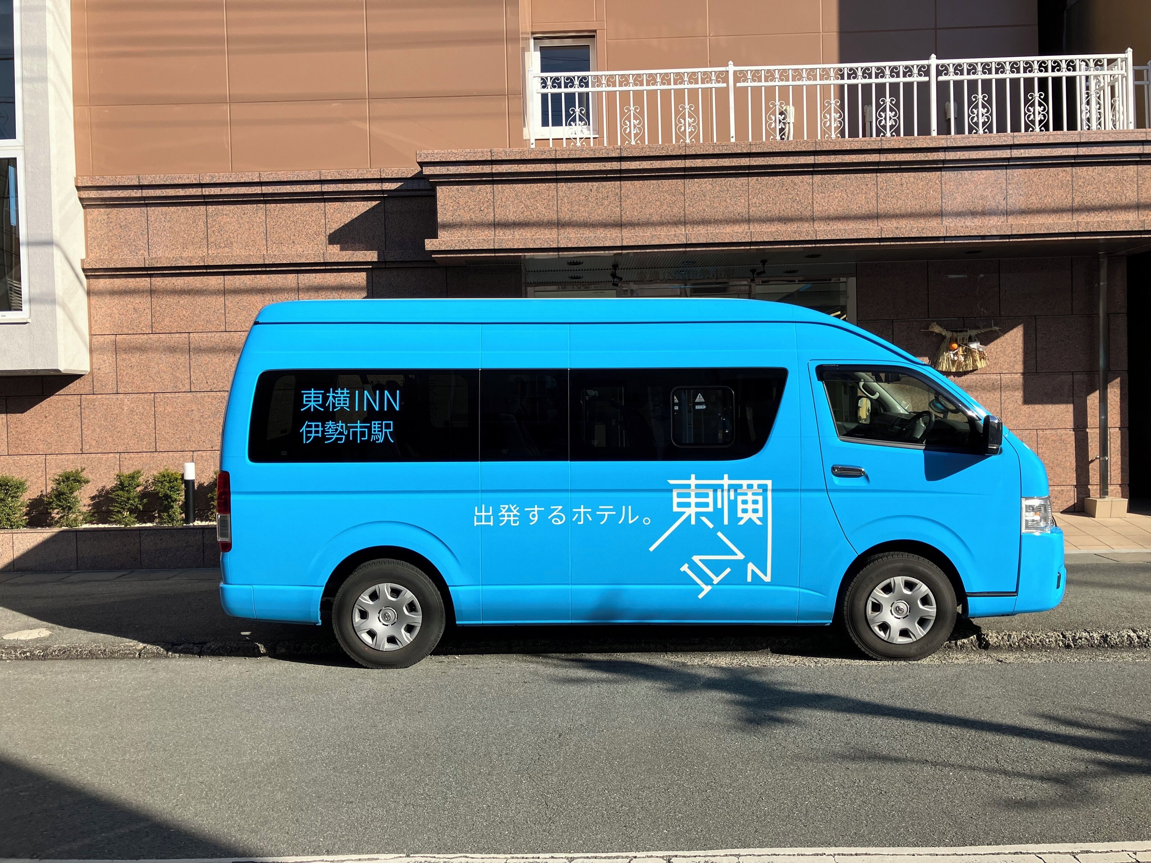 A blue van parked in front of a building with a balcony.