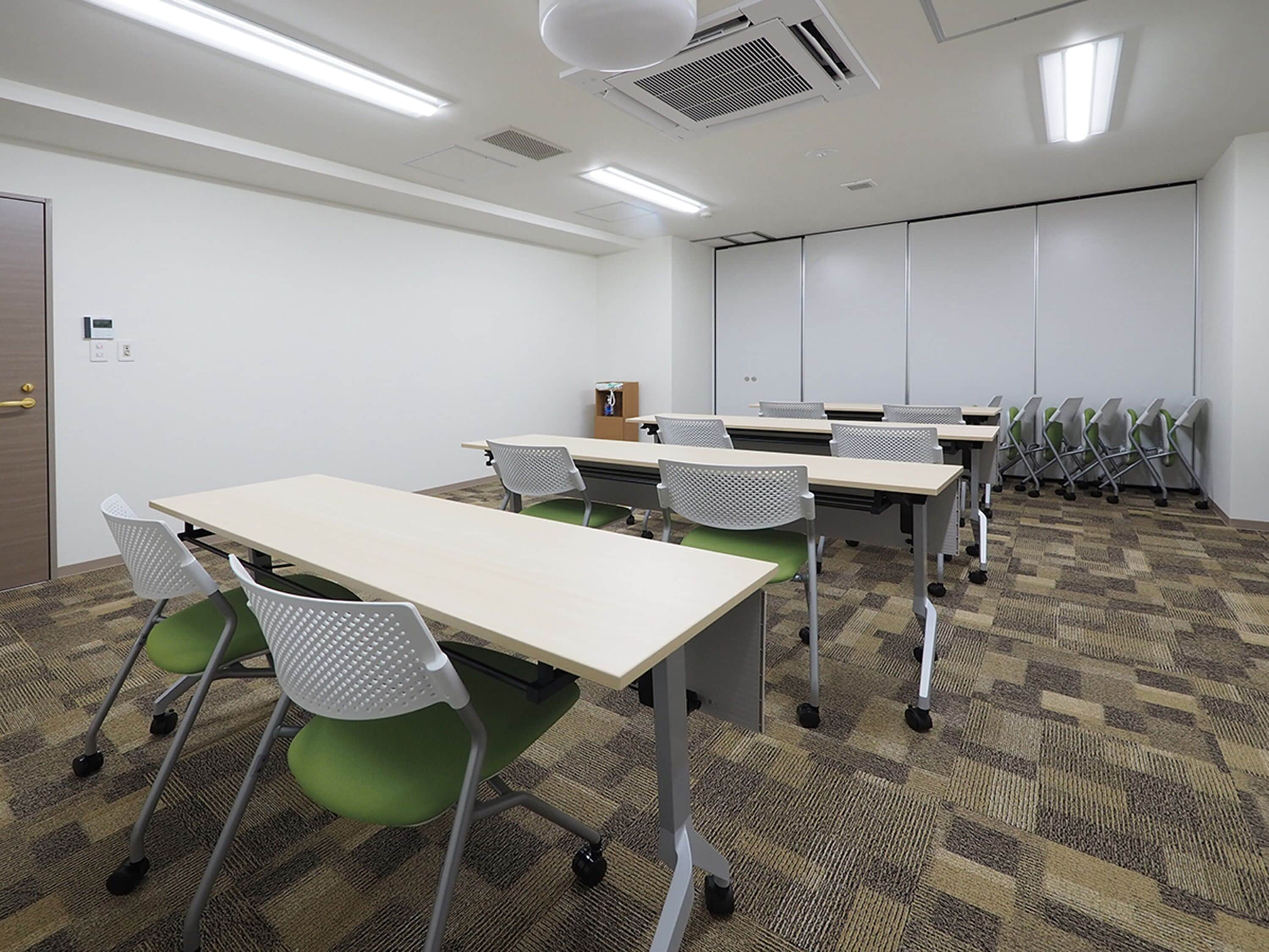 A conference room with tables and chairs, carpeted floor, white walls, and ceiling lights.