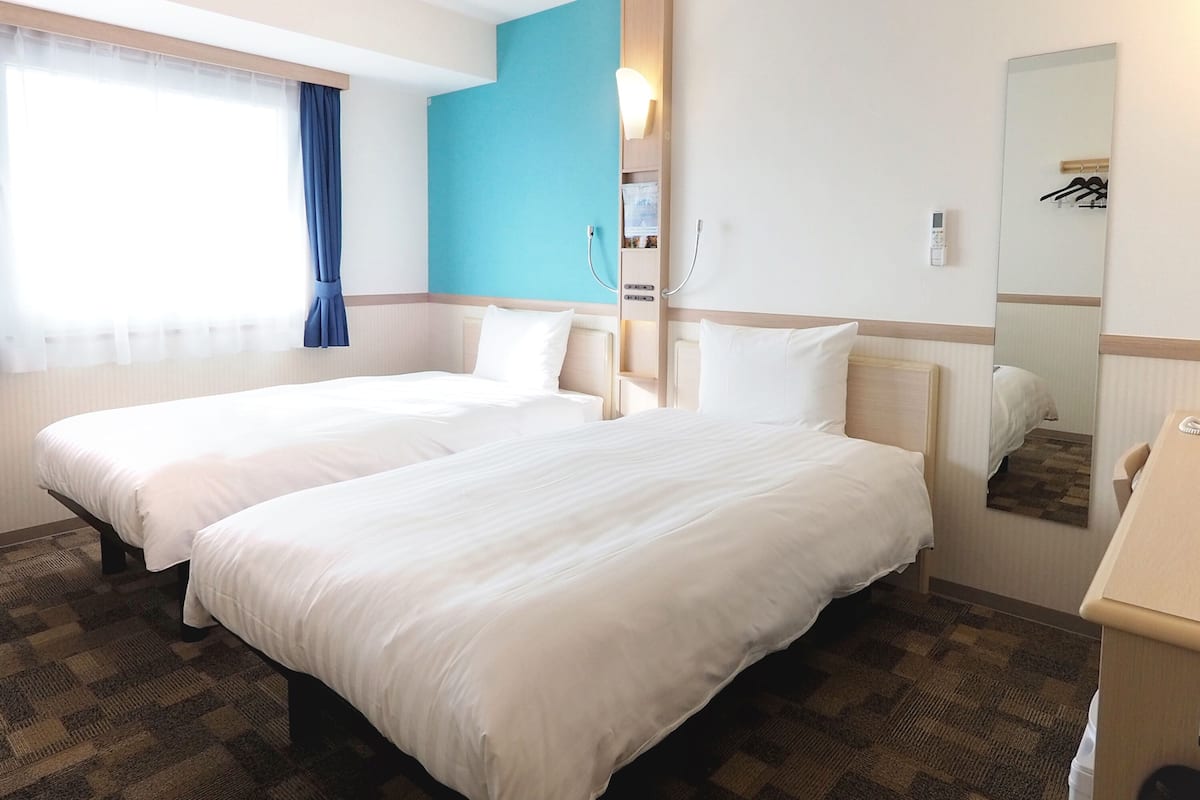 Une chambre d’hôtel avec deux lits, une salle de bain, un miroir et une fenêtre avec des rideaux.