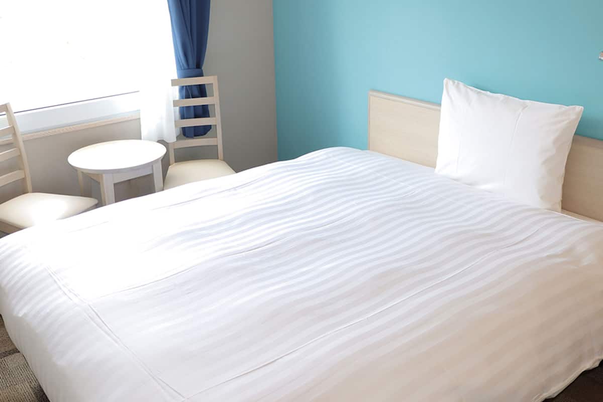 Une chambre d’hôtel avec un lit, une chaise, une petite table ronde et une fenêtre avec des rideaux.